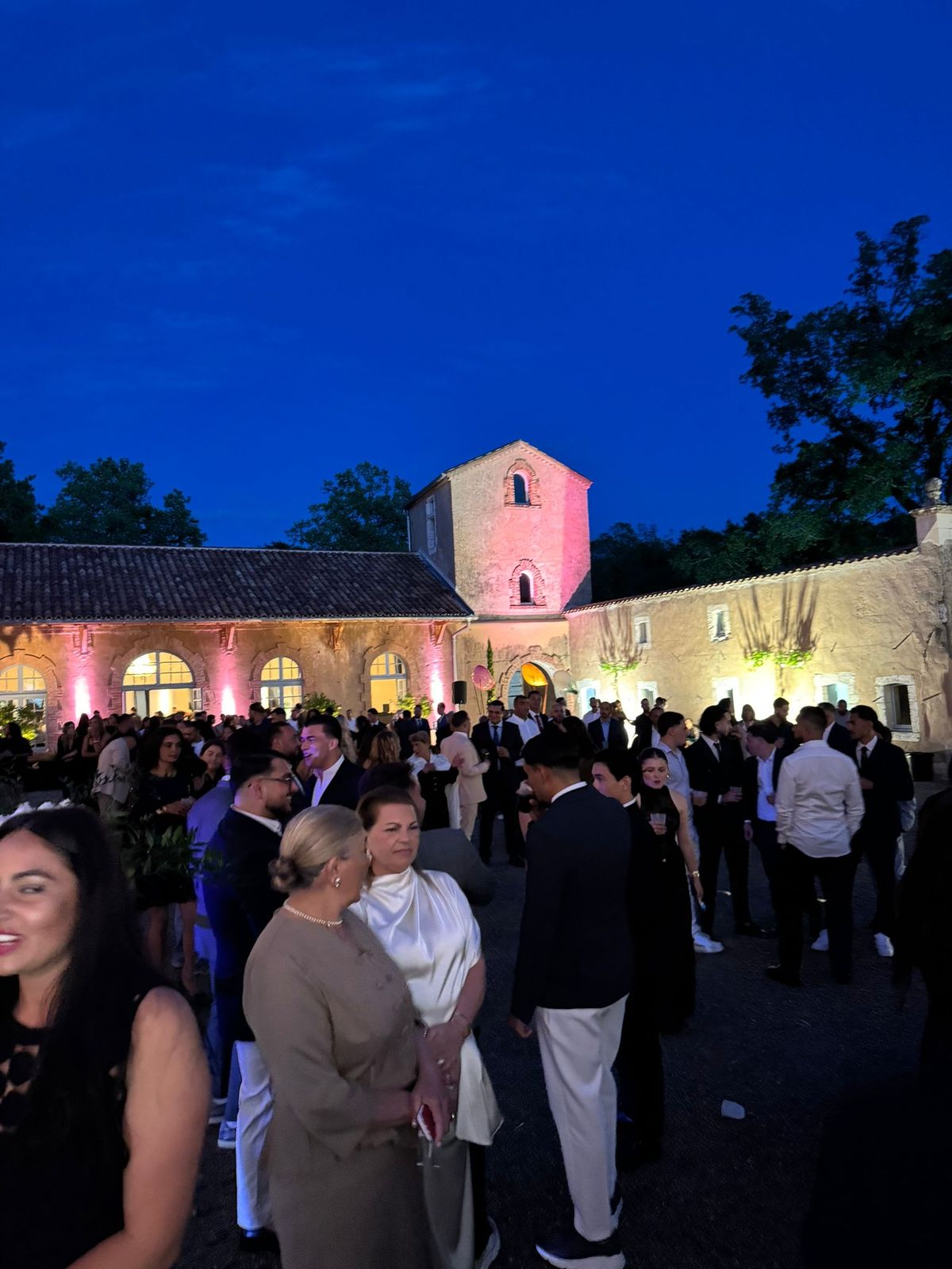 Guests gathered at night in the château courtyard for a wedding reception, the building lit in pink uplighting.