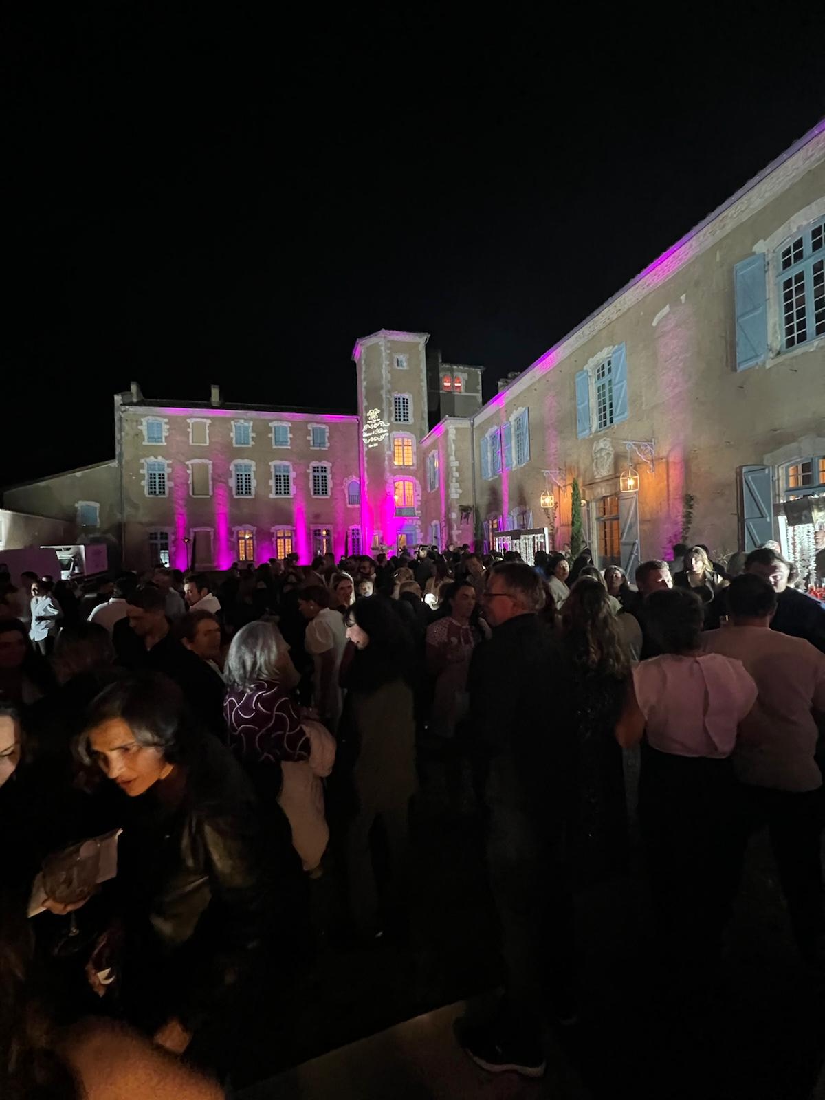 Guests gathered for an evening cocktail reception in the château courtyard, the building lit in pink.