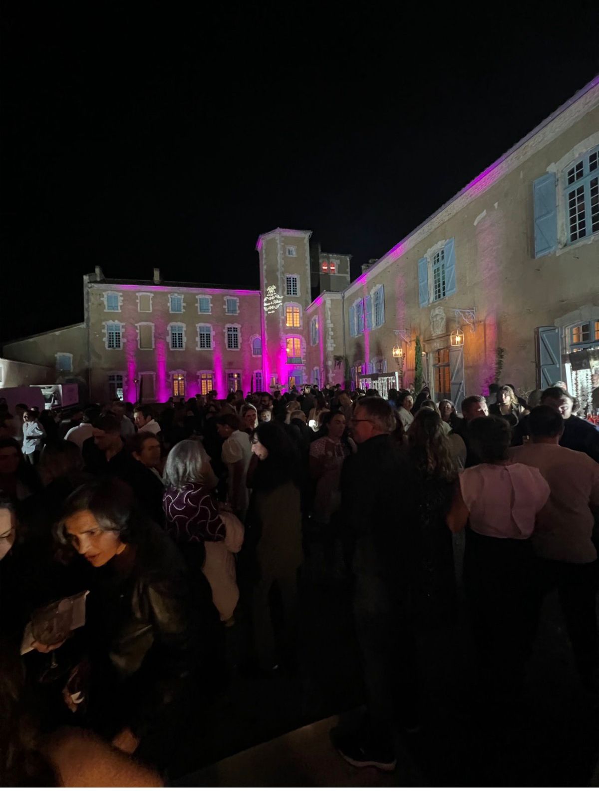 Guests gathered at night in the château courtyard for a reception, the building lit in pink and purple.