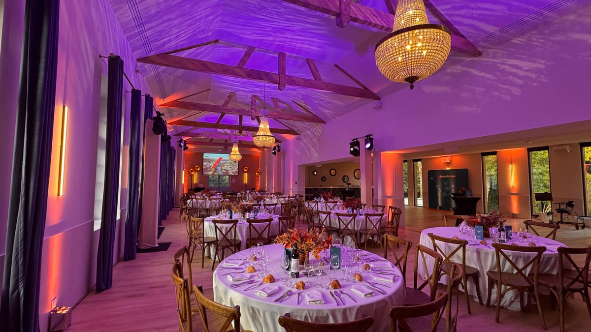 The Orangerie set for a formal dinner with round tables, lit in purple and orange under a beamed ceiling.