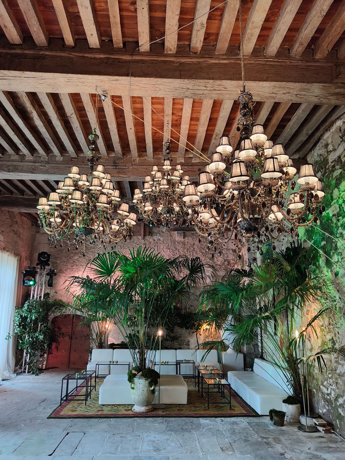 A stone-walled lounge with tiered chandeliers, potted palms and white modular seating.
