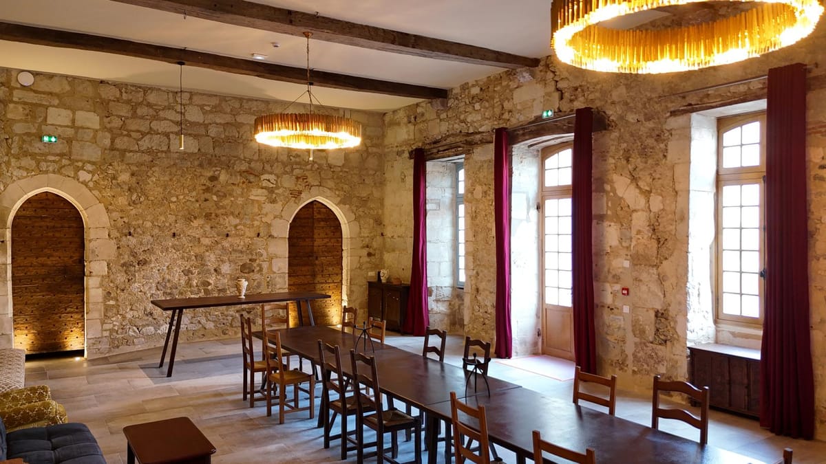 A long dining table set for a meal in a stone-walled hall with arched doorways and pendant lighting.