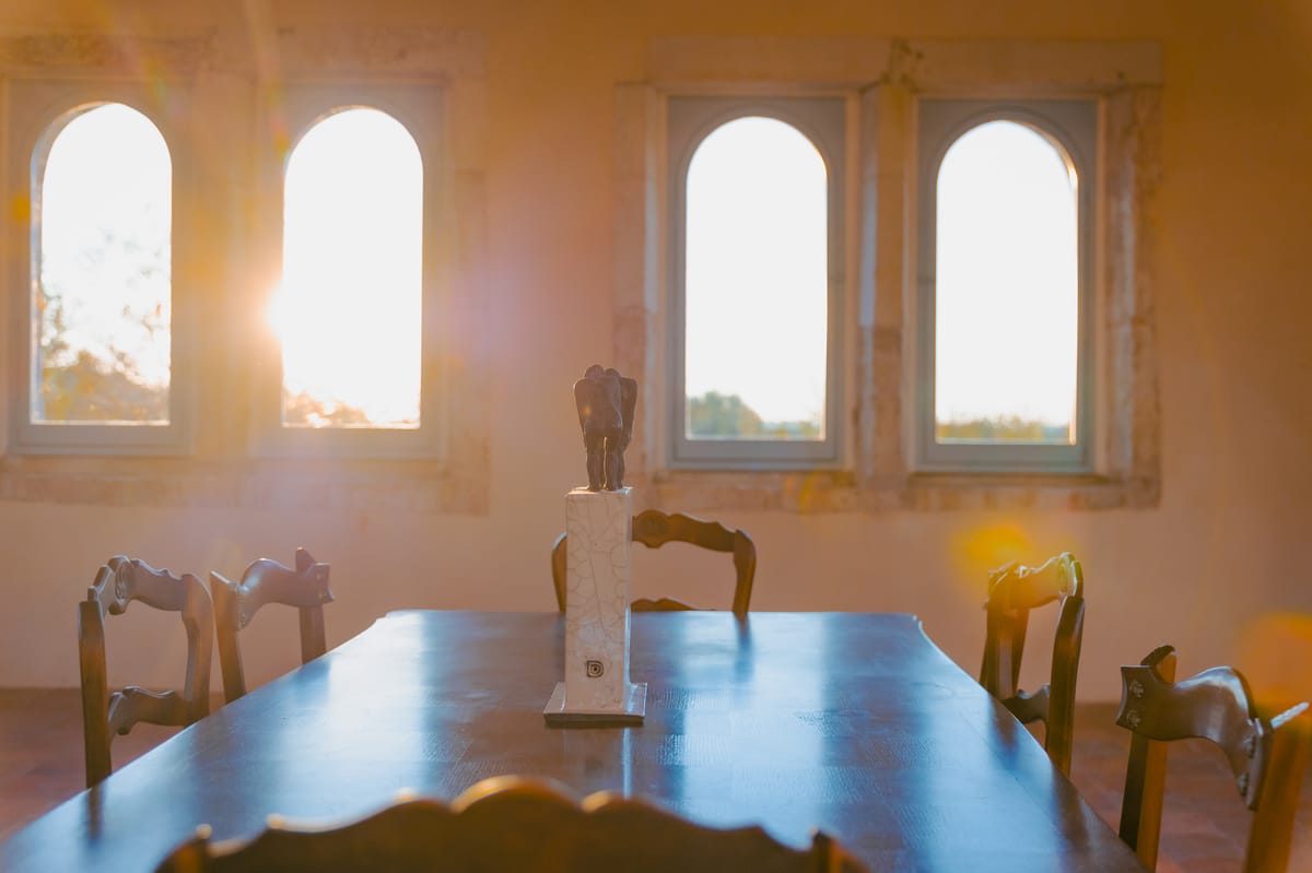 A sunlit room with arched windows and a wooden table set with a small sculpture.