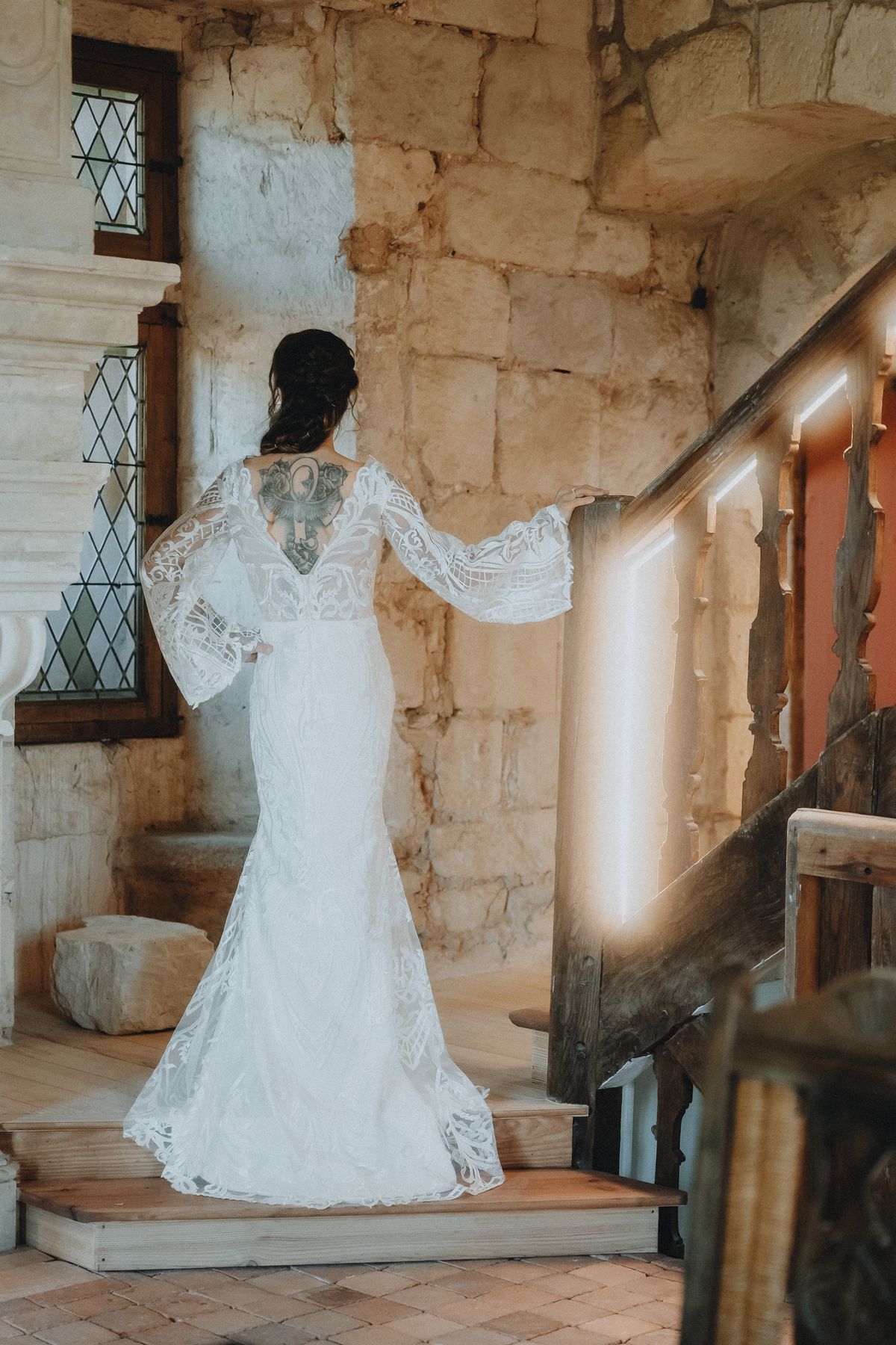 A bride in a lace gown standing on a stone staircase inside the château's tower.