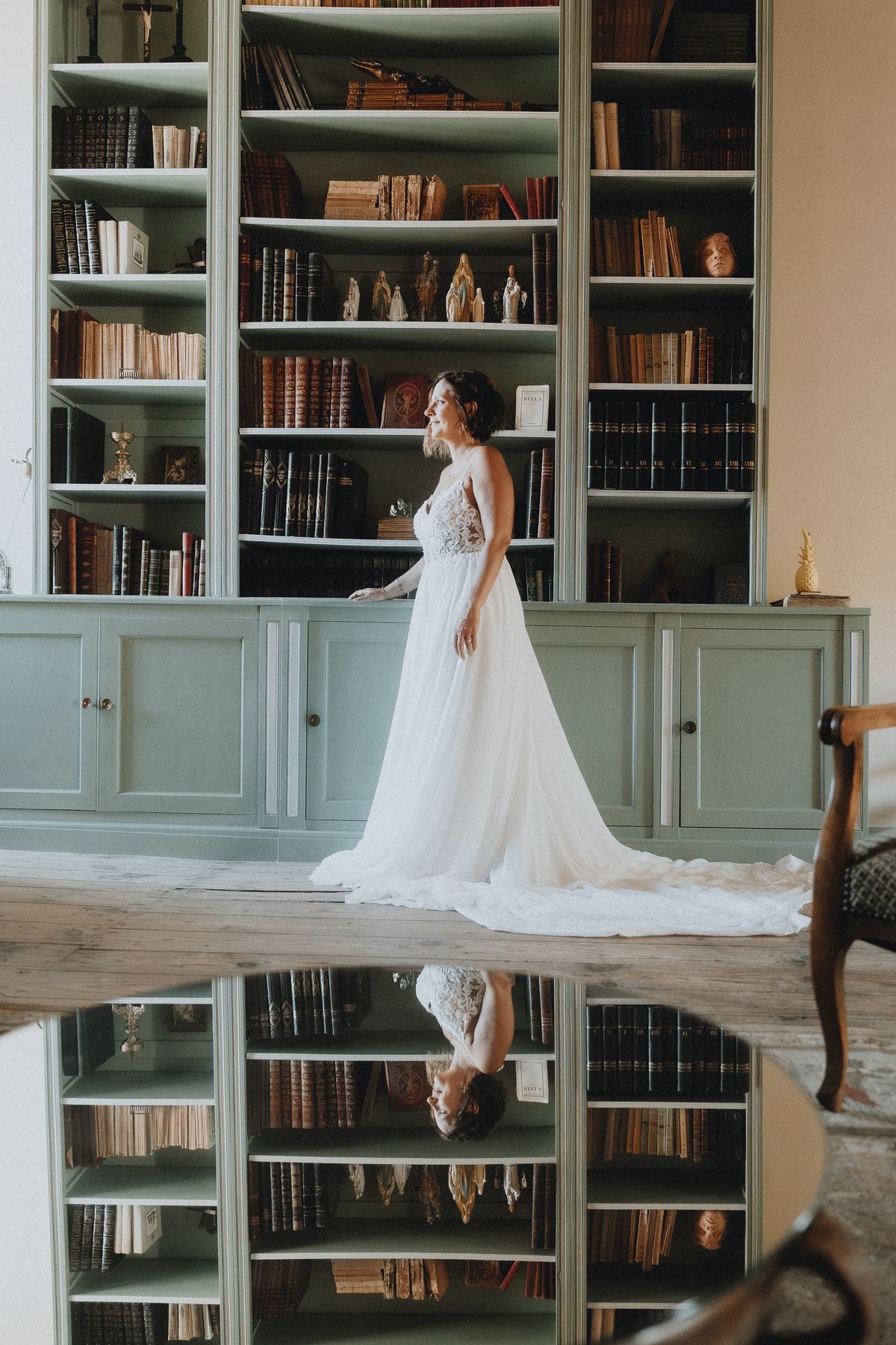 A bride in a white gown standing in front of built-in bookshelves in the château's library.