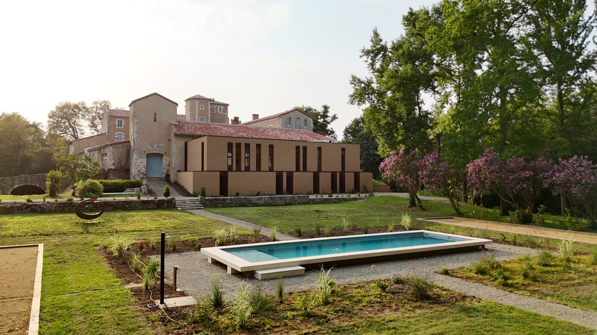The swimming pool and lawn in front of the château's modern extension building at golden hour.