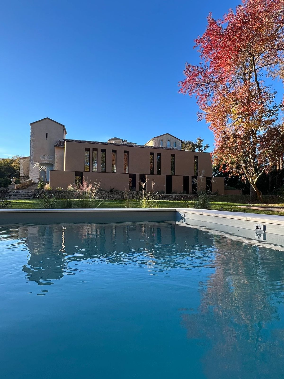 The swimming pool in front of the château's modern extension building, with an autumn tree in the foreground.