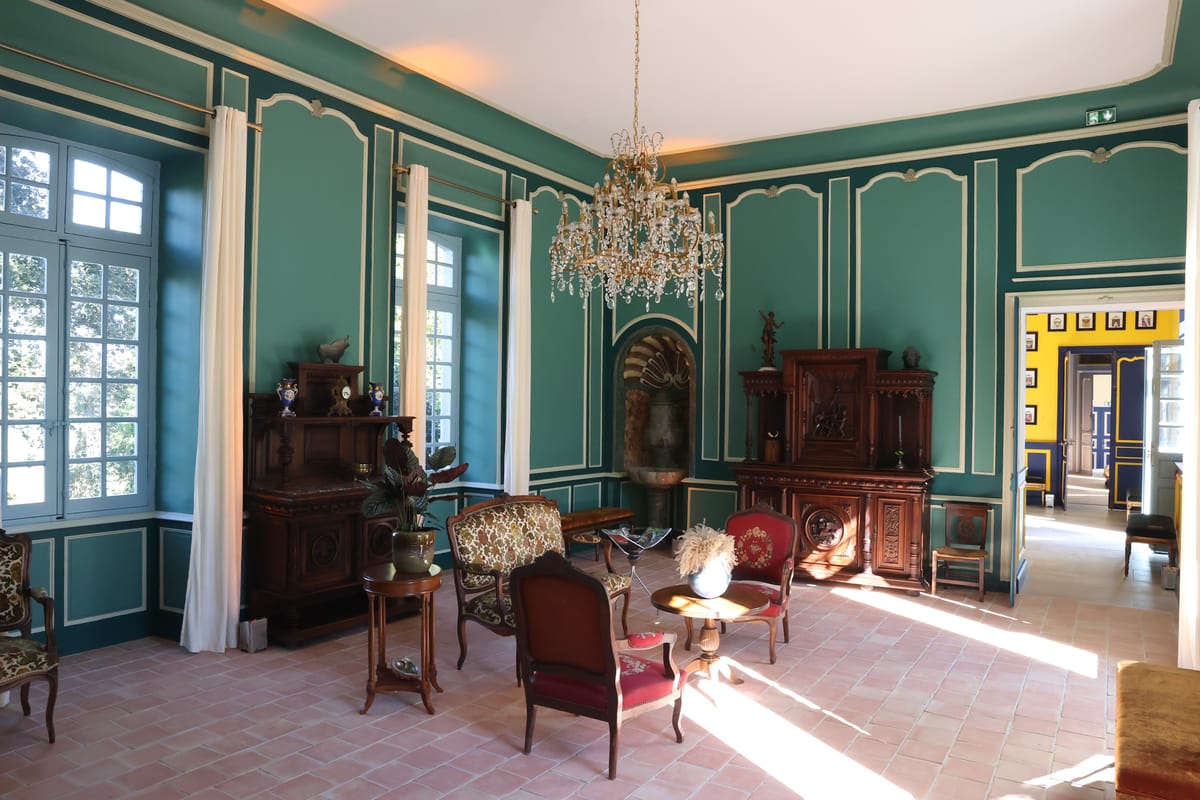 A green-panelled salon with a crystal chandelier, antique cabinets and armchairs, opening to a yellow room beyond.