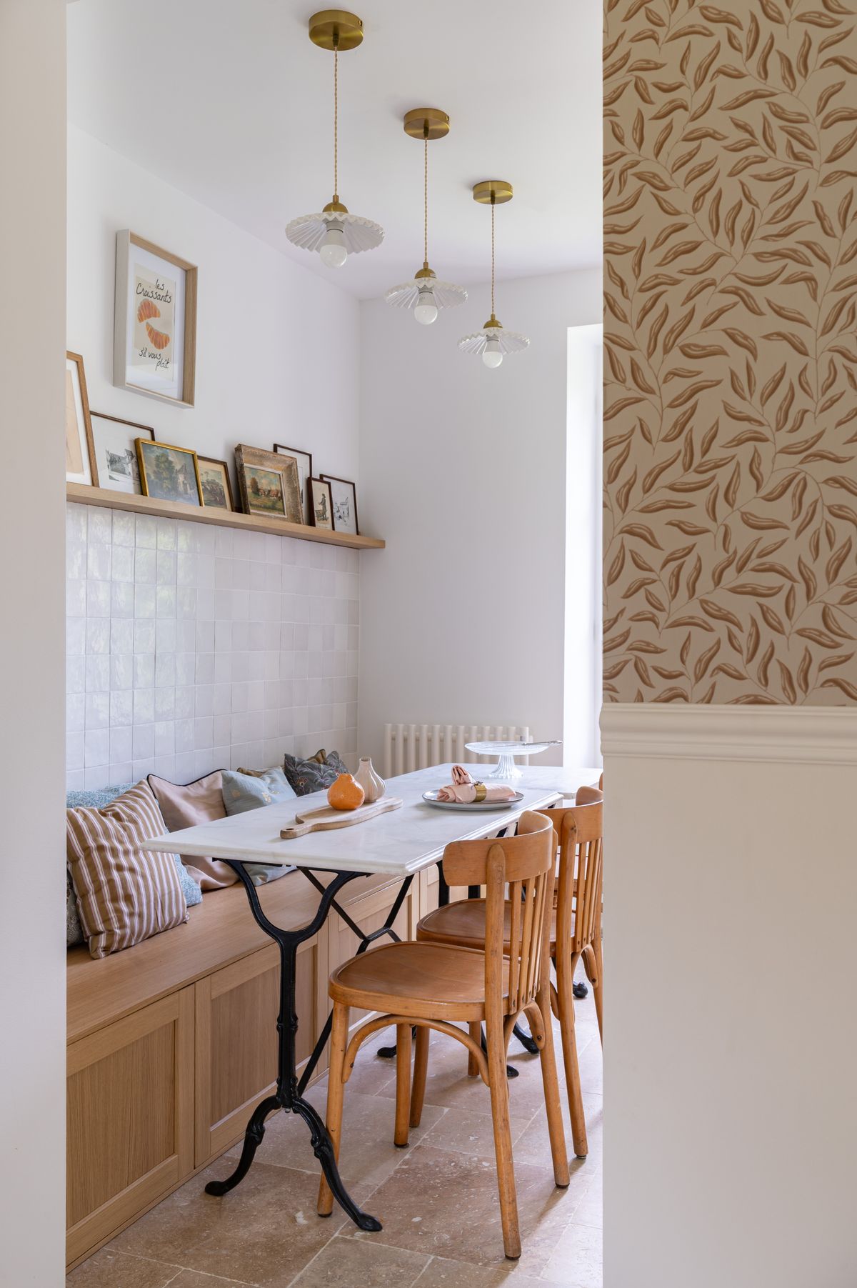 A breakfast corner with a marble bistro table, bentwood chairs and a banquette under three glass pendants
