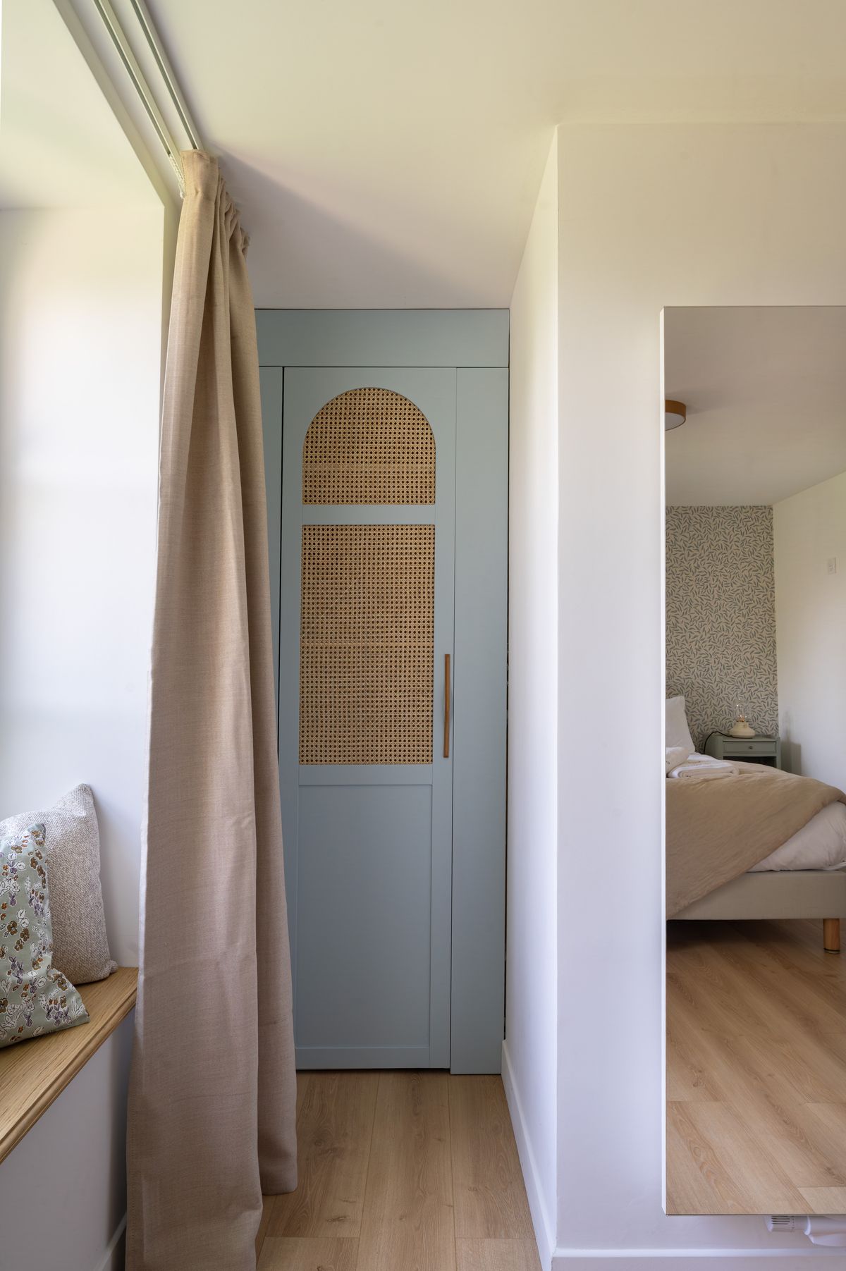 A guest house landing with a cane-fronted wardrobe and a mirror reflecting the bedroom beyond