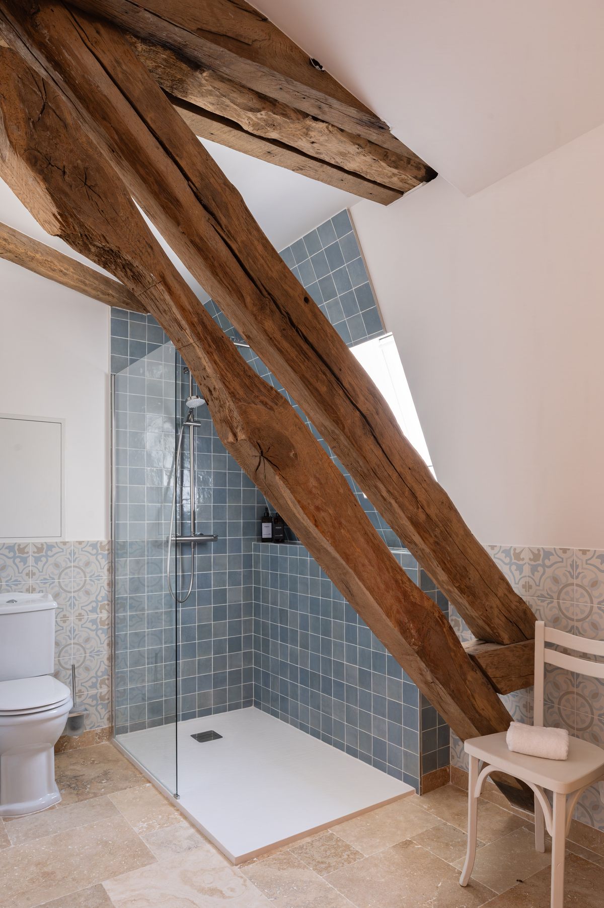 A bathroom under exposed oak beams, with a blue-tiled walk-in shower and patterned tiles round the walls
