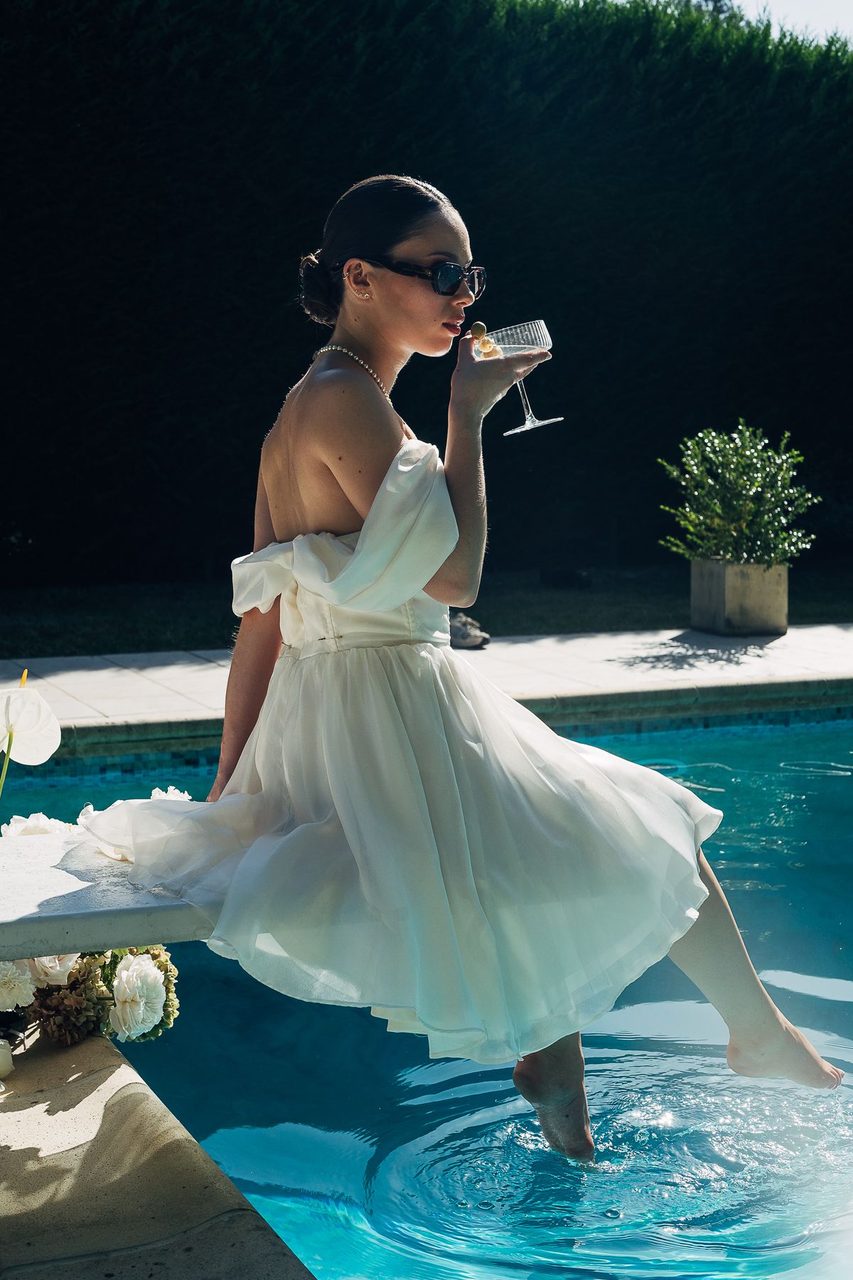 A bride in an off-the-shoulder gown on the diving board, a coupe in hand and one foot in the pool