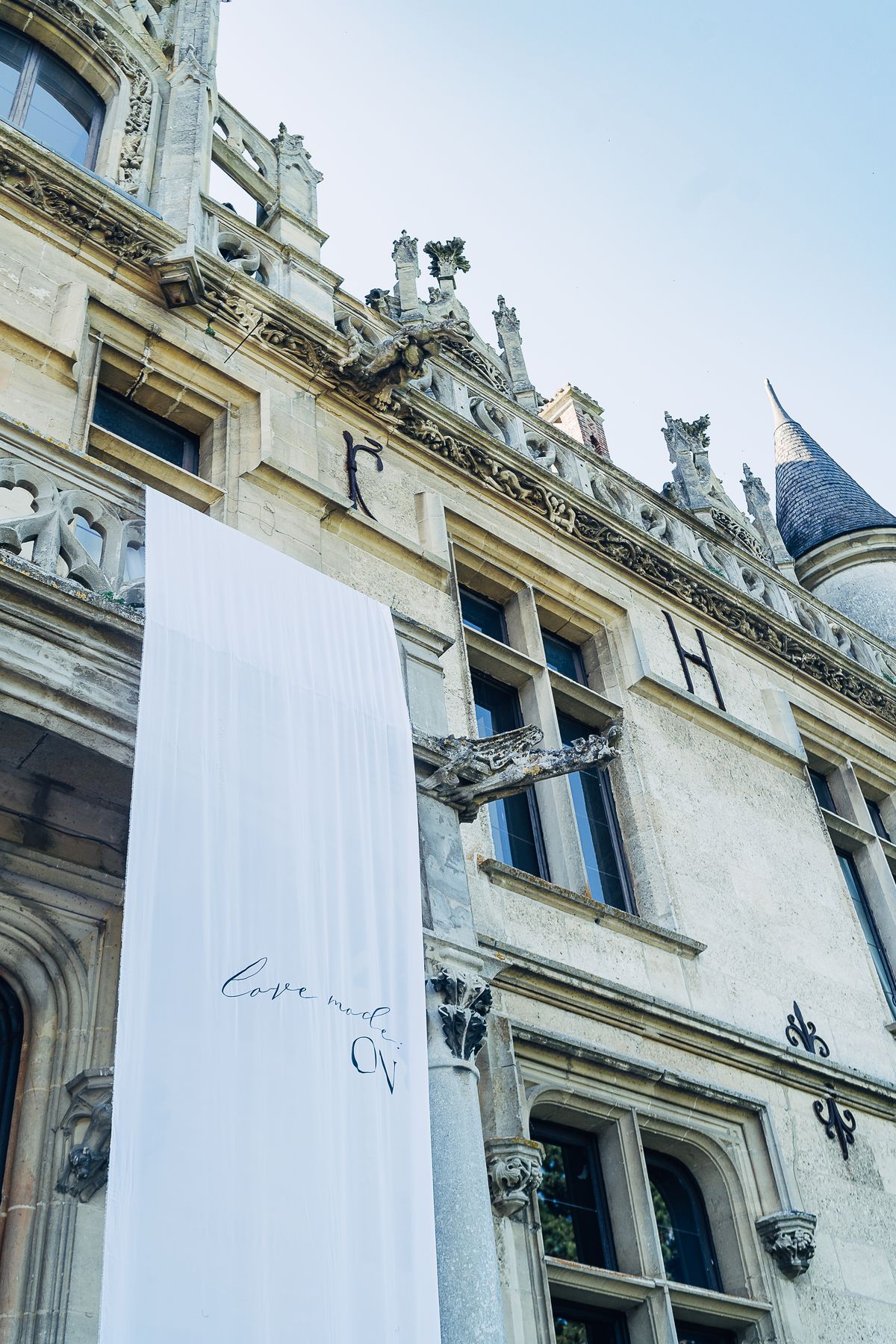 Carved gargoyles and pinnacles along the château's upper facade, with a white banner hung by the entrance