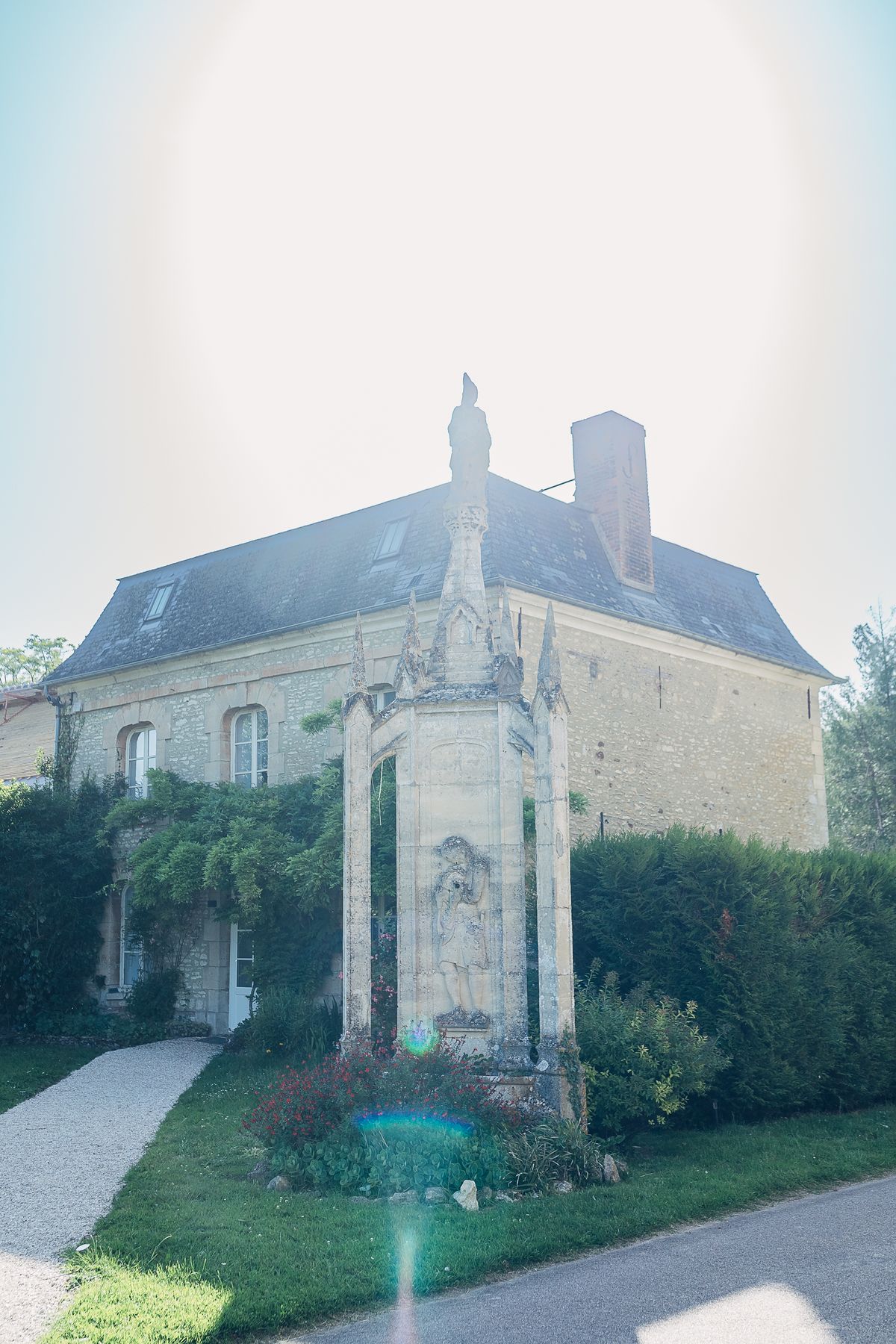 The guest house exterior with its carved stone monument and climbing greenery, beside the gravel path