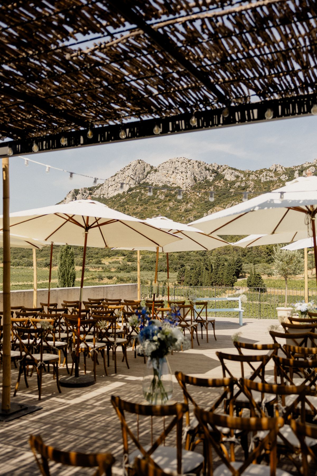 Ceremony chairs under the reed pergola and white parasols on the terrace at Domaine ODDO Vallon des Glauges, with the limestone hills of the Alpilles beyond