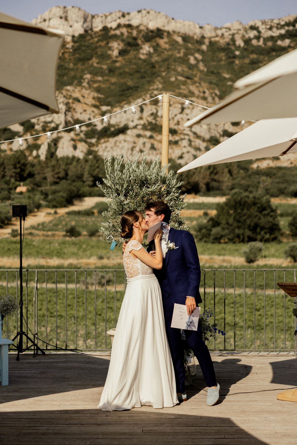 A couple kiss during their ceremony on the terrace at Domaine ODDO Vallon des Glauges, with vineyards and the Alpilles behind