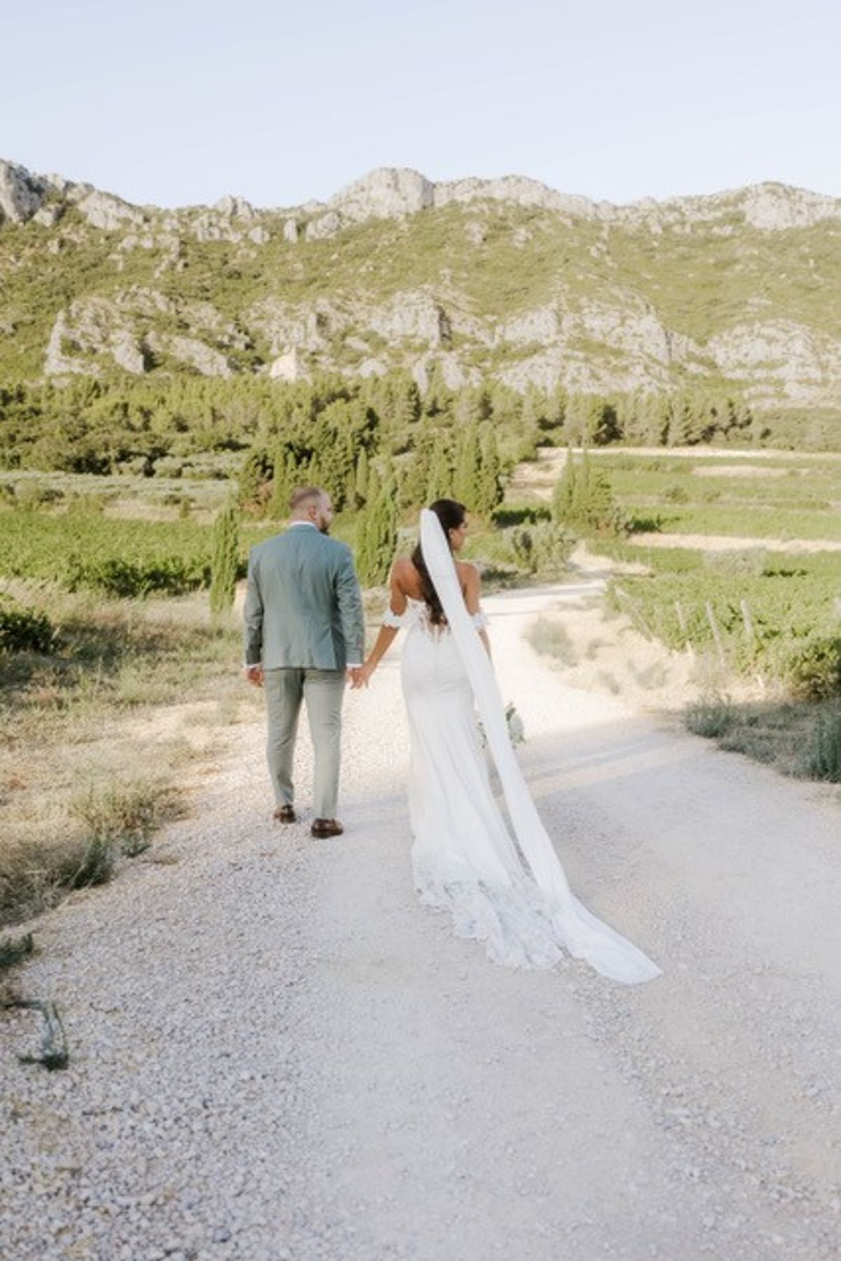 A couple walk hand in hand along a track between the vines at Domaine ODDO Vallon des Glauges, with the Alpilles ahead