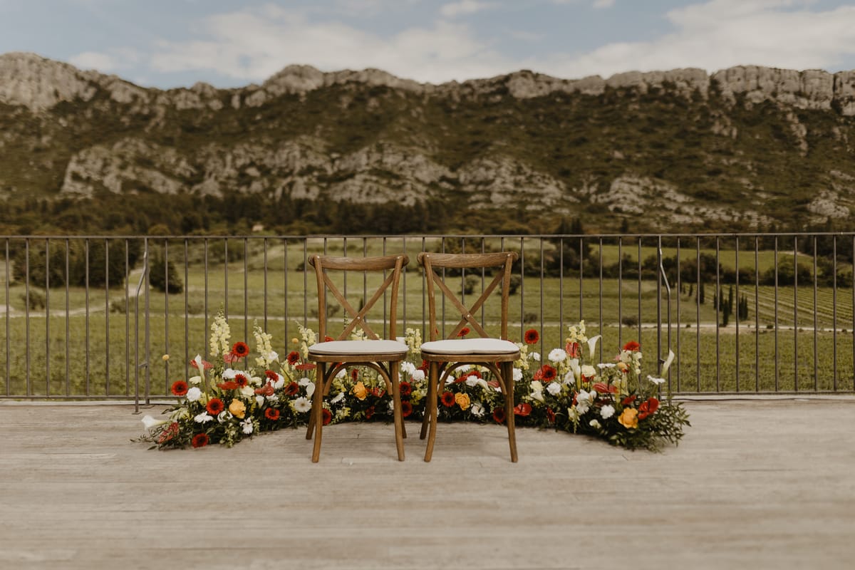 Two wooden chairs framed by red and white flowers on the terrace at Domaine ODDO Vallon des Glauges, looking over the vineyards to the Alpilles