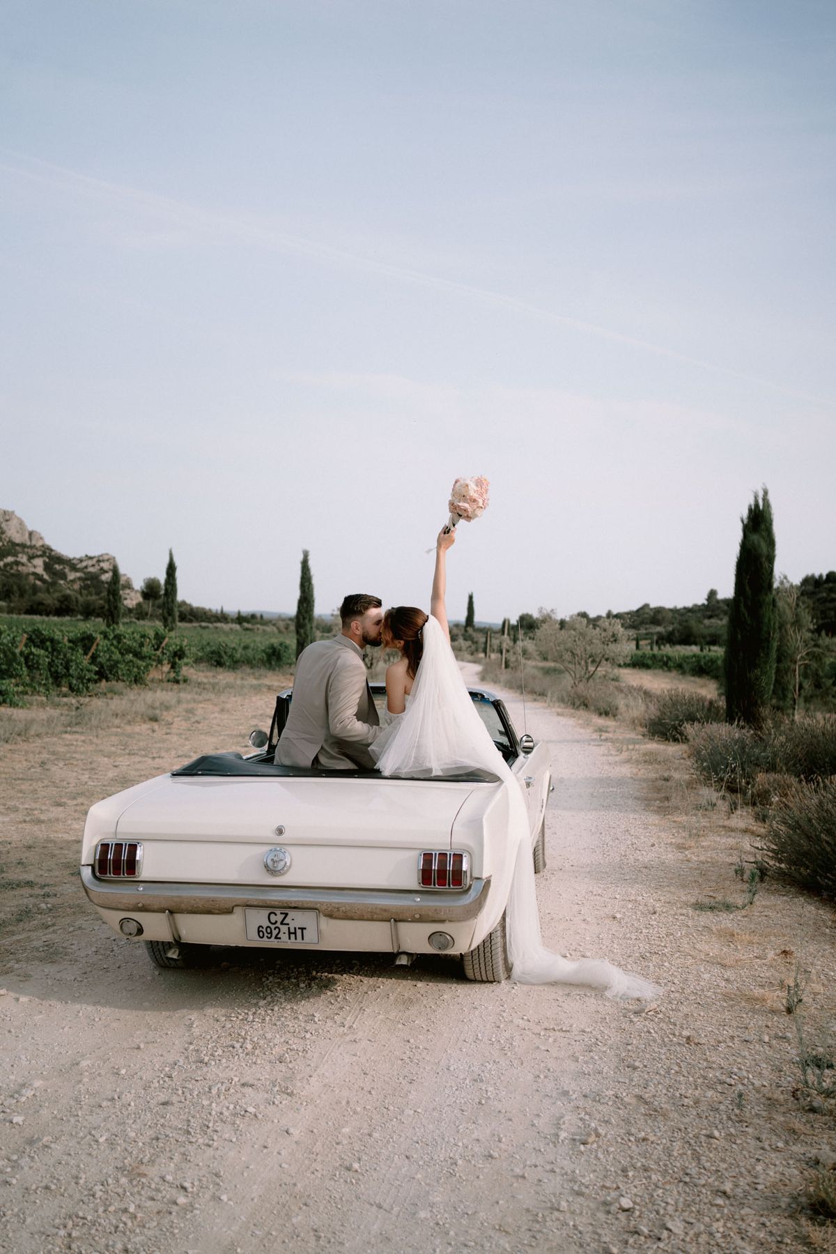 A couple in a white vintage convertible on a track lined with cypress trees near Domaine ODDO Vallon des Glauges