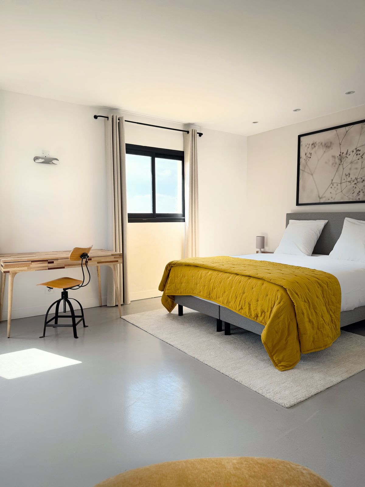 A bright bedroom at the Villa des Glauges with a mustard throw, a writing desk and a framed map