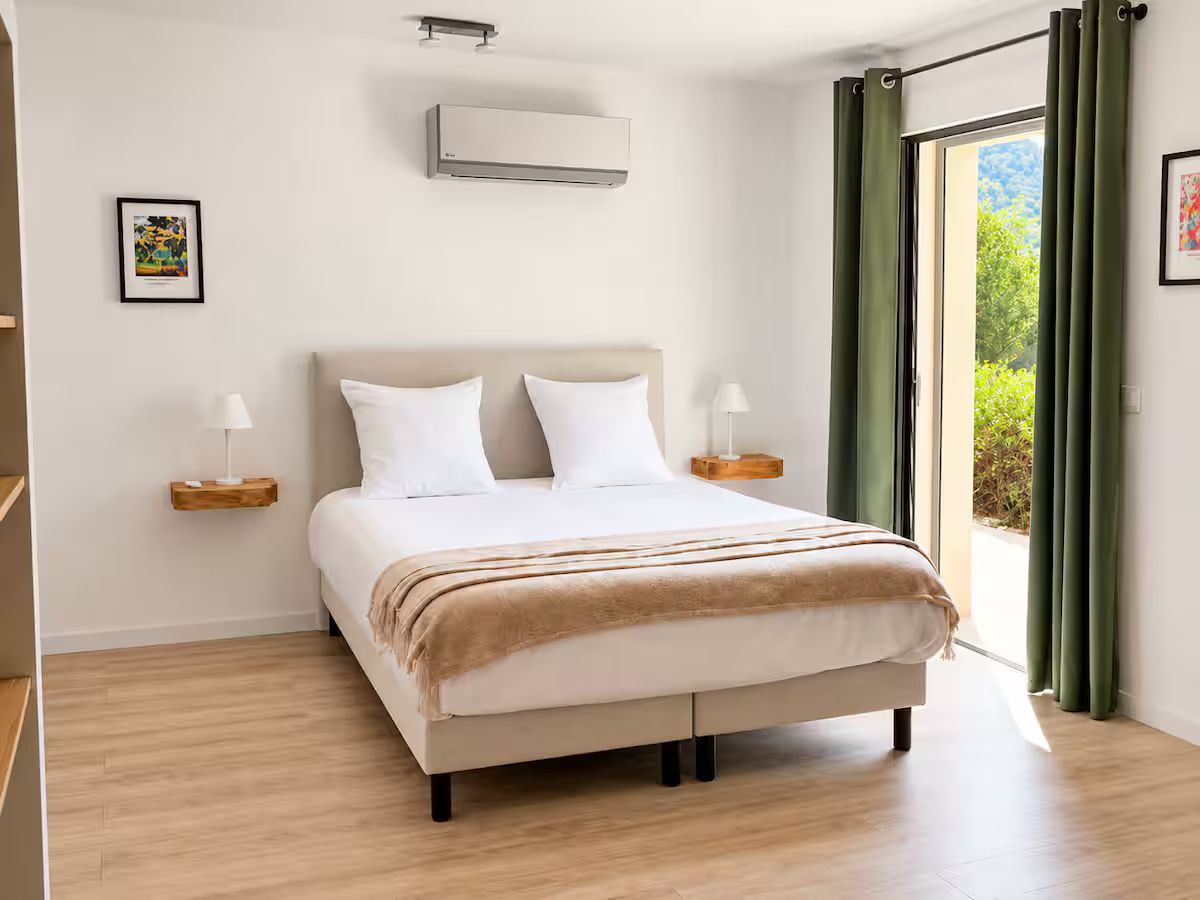 A double bedroom at the Villa des Glauges with green curtains, air conditioning and a door opening to the garden