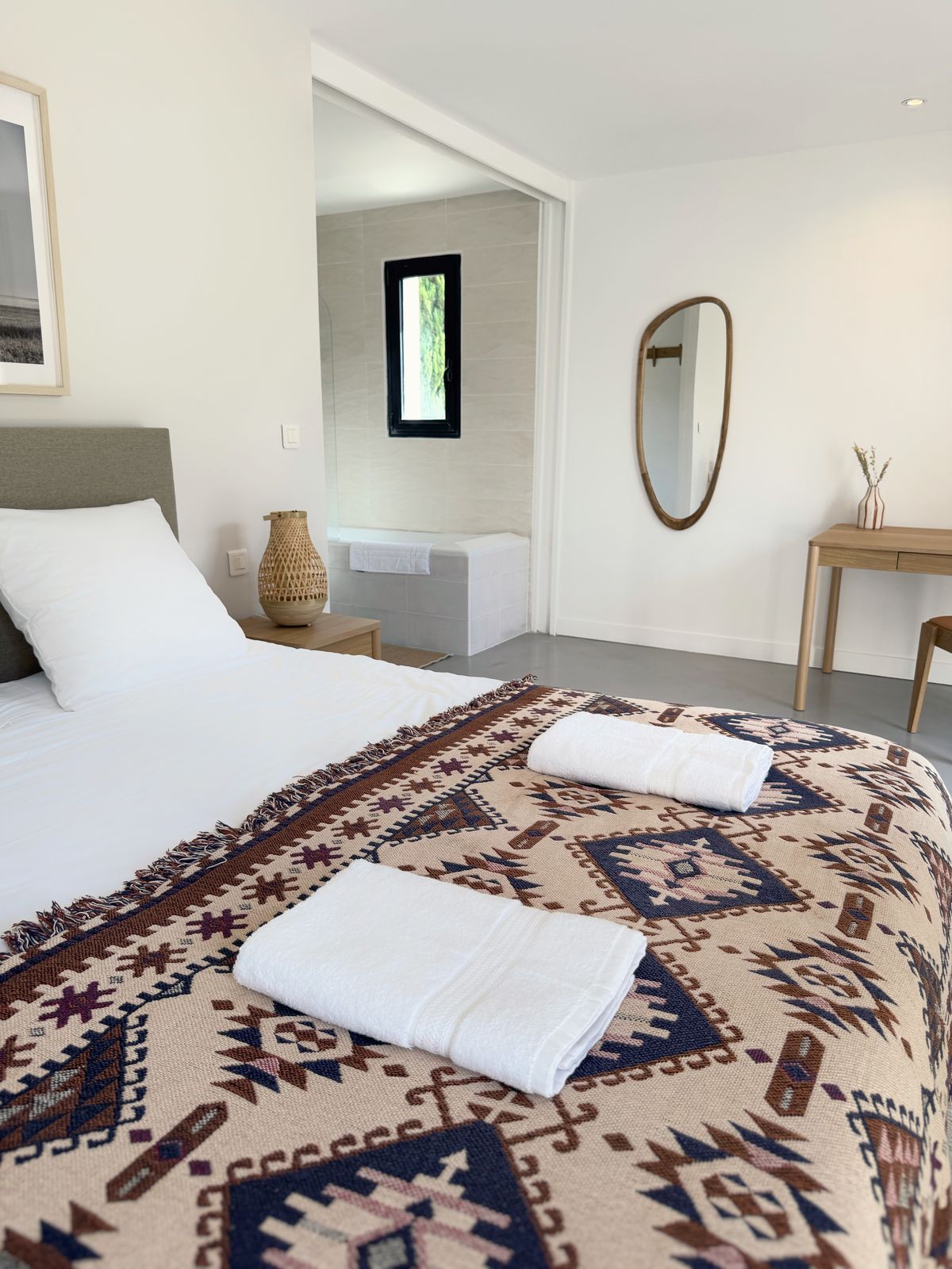 A bedroom at the Villa des Glauges with a patterned throw, fresh towels and an oval mirror