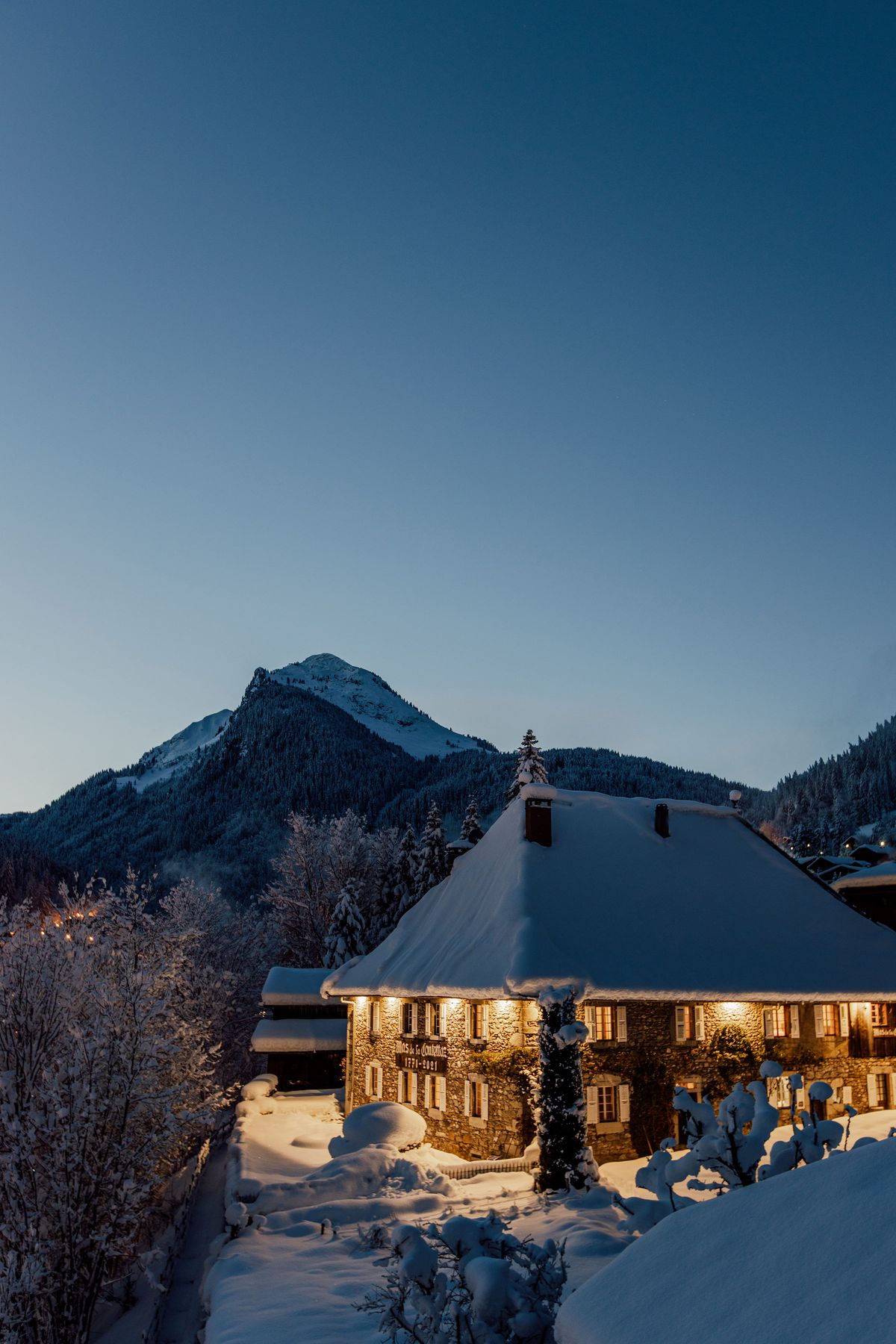 Hotel Coutettaz under snow at dusk, with snow-covered mountains behind