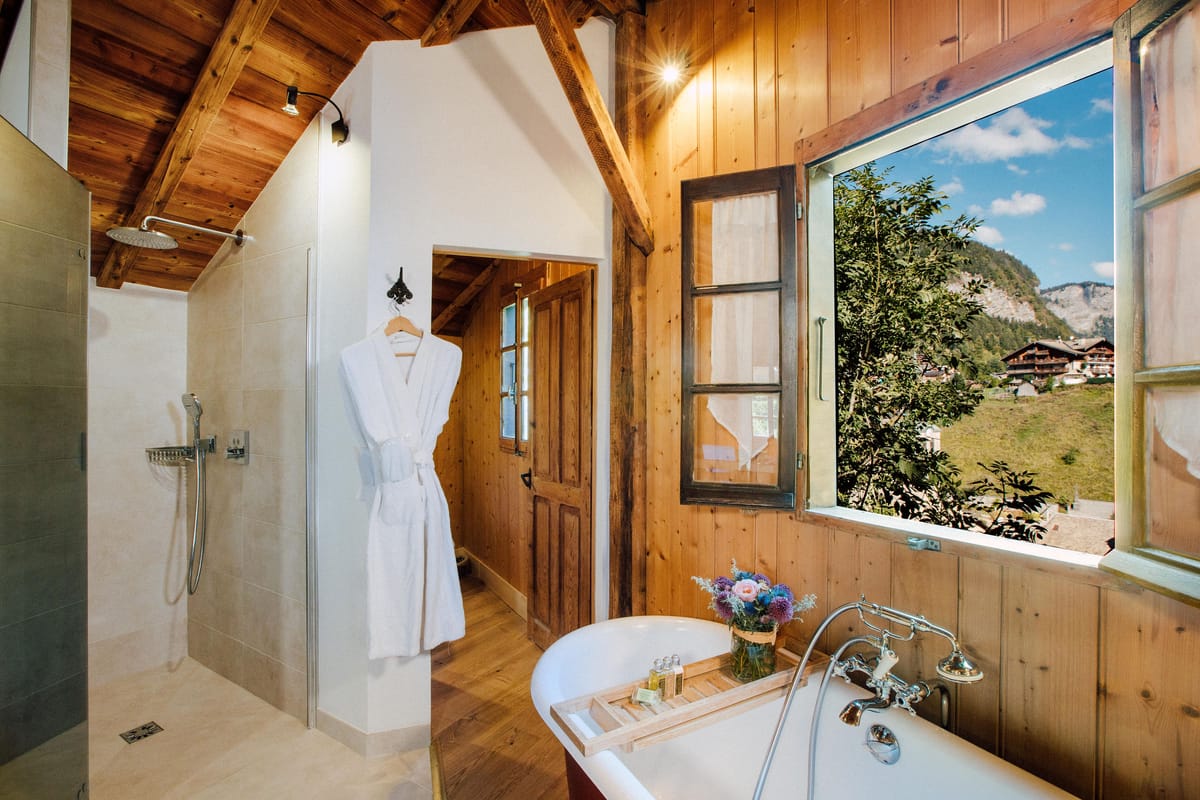 Wood-panelled bathroom with a roll-top bath under a window looking out to the mountains