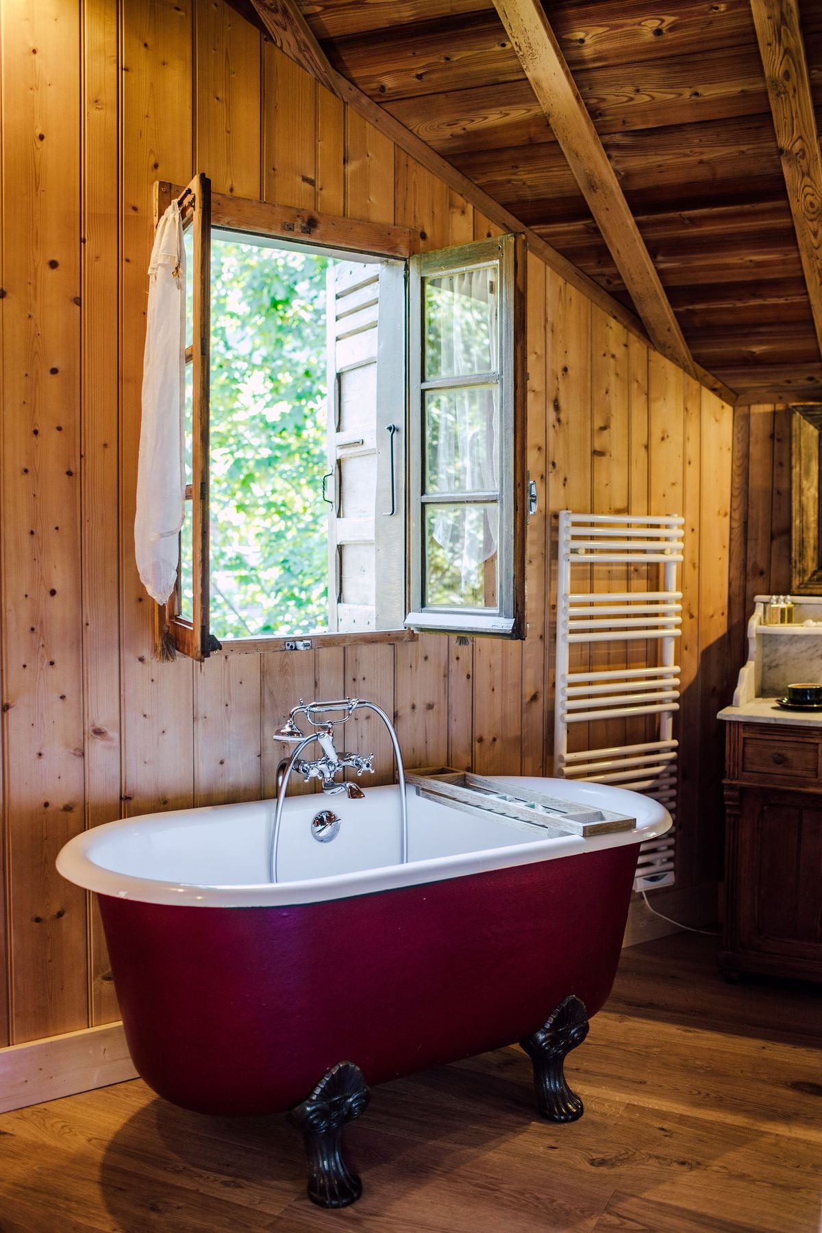 Red roll-top bath in a wood-panelled bathroom