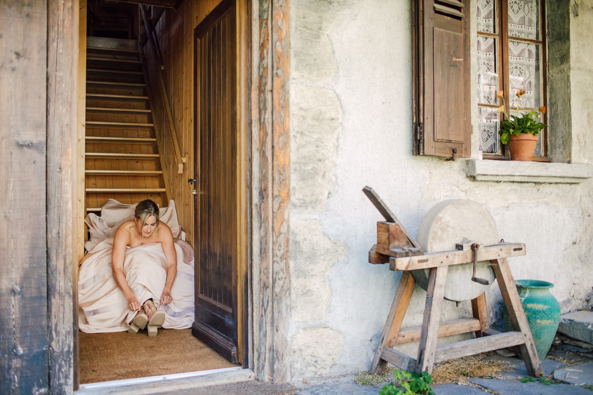 Bride putting on her shoes in the doorway of an old outbuilding, beside a grindstone