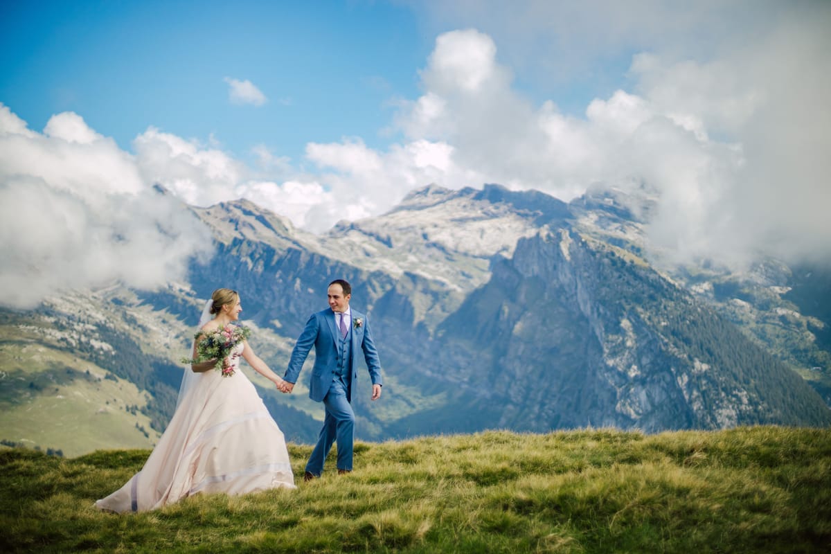 Bride and groom walking across a mountain meadow
