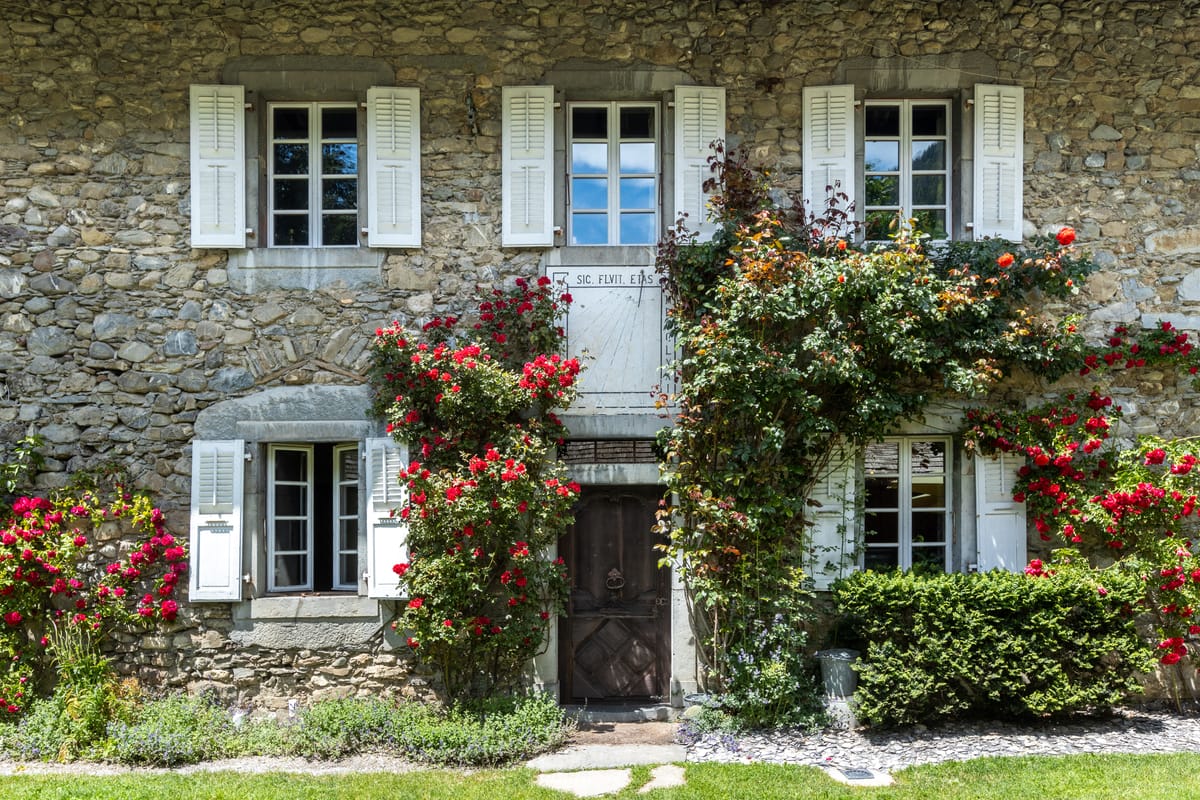 Stone facade of Hotel Coutettaz with white shutters and climbing roses