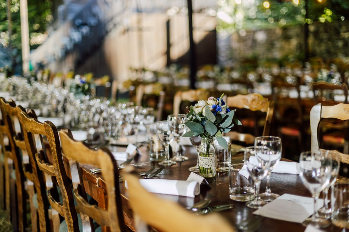 Long tables with wooden chairs, glasses and posies of flowers set for dinner