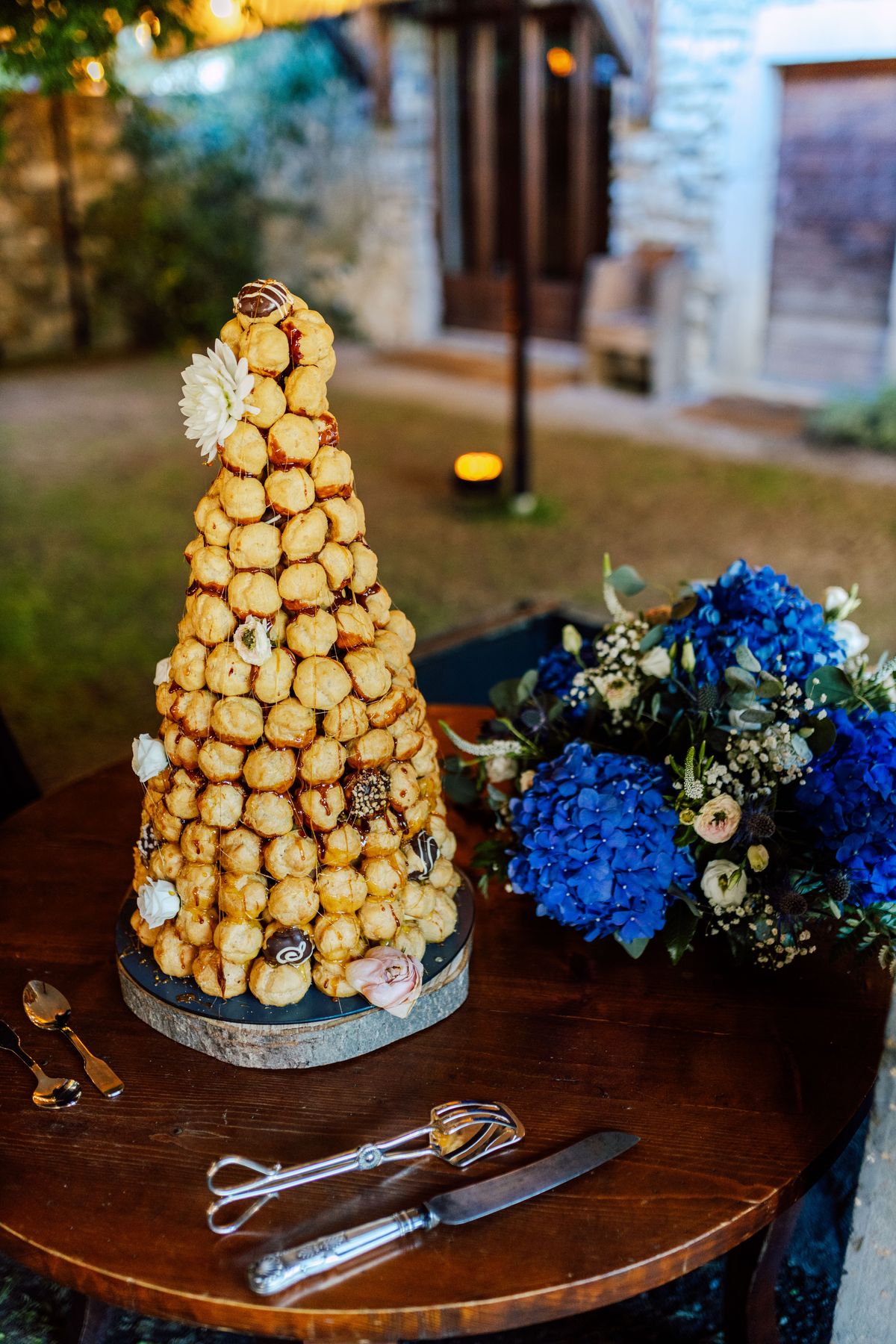 Croquembouche beside blue hydrangeas on a table in the garden