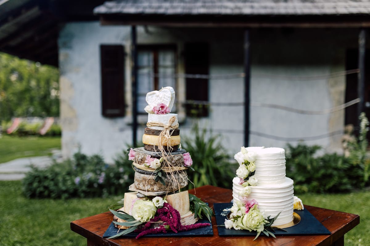 A tower of cheese wheels and a tiered wedding cake on a table in the garden