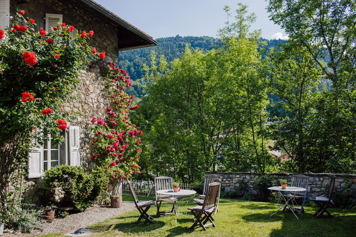 Garden tables and chairs beside the stone house and climbing roses, with mountains behind