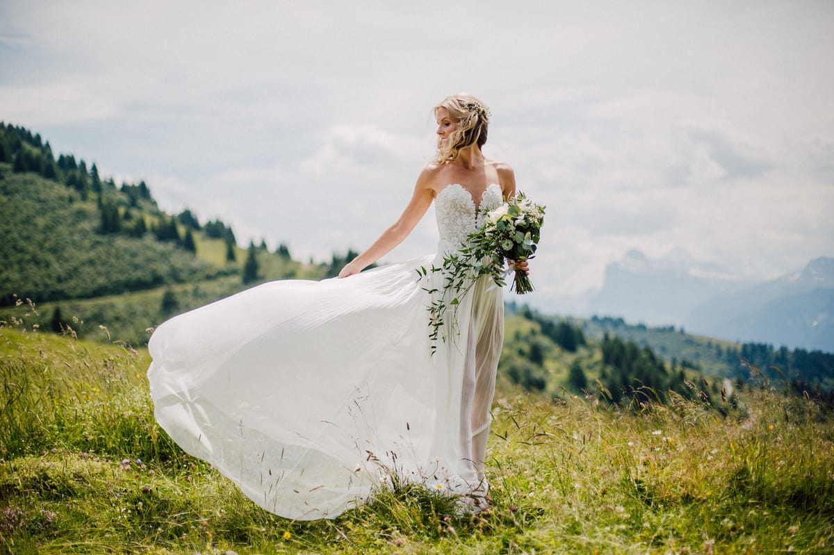 Bride in a mountain meadow, her skirt caught by the wind
