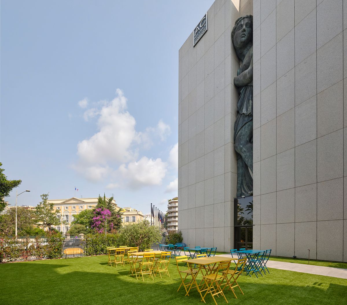 Garden of Montcalm Nice with yellow and blue bistro tables beside the hotel façade and its Venus sculpture