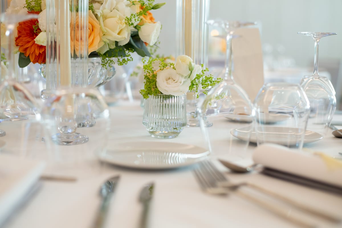 Wedding table with white roses in ribbed glass vases and stemmed glasses