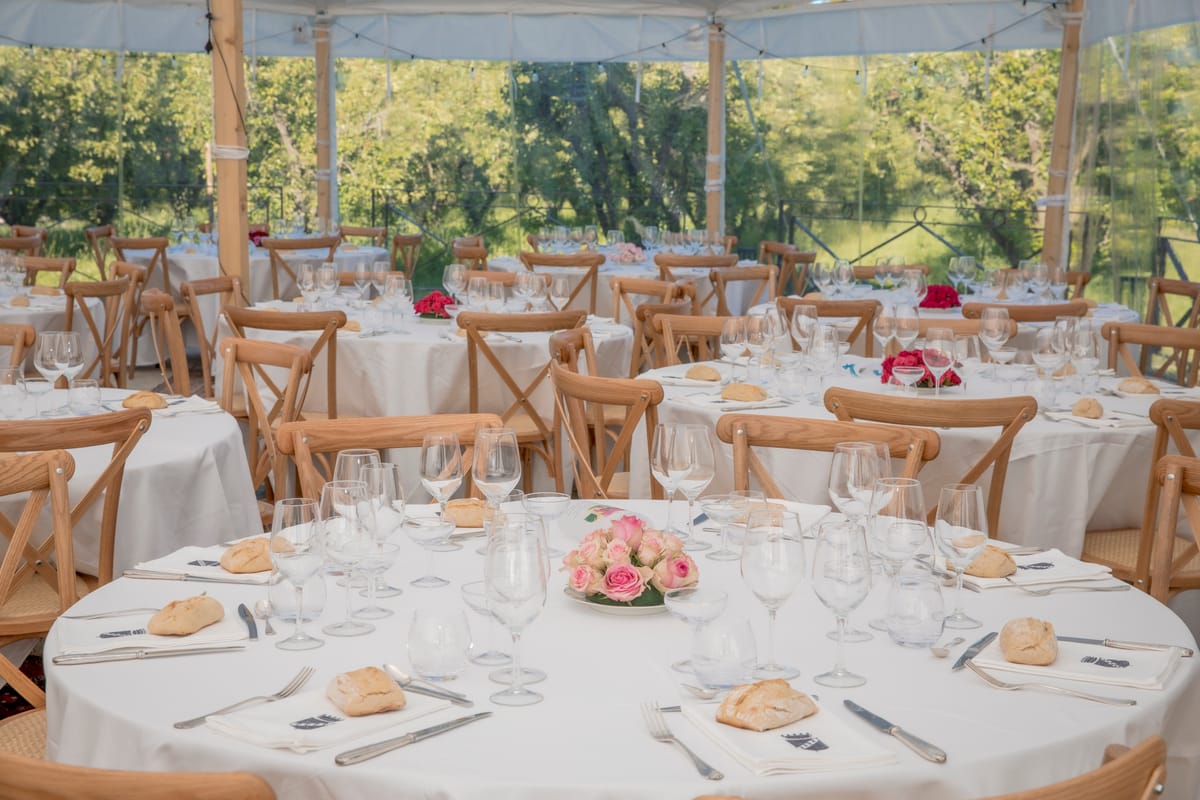 Round tables set for dinner under the sailcloth marquee, string lights and garden view