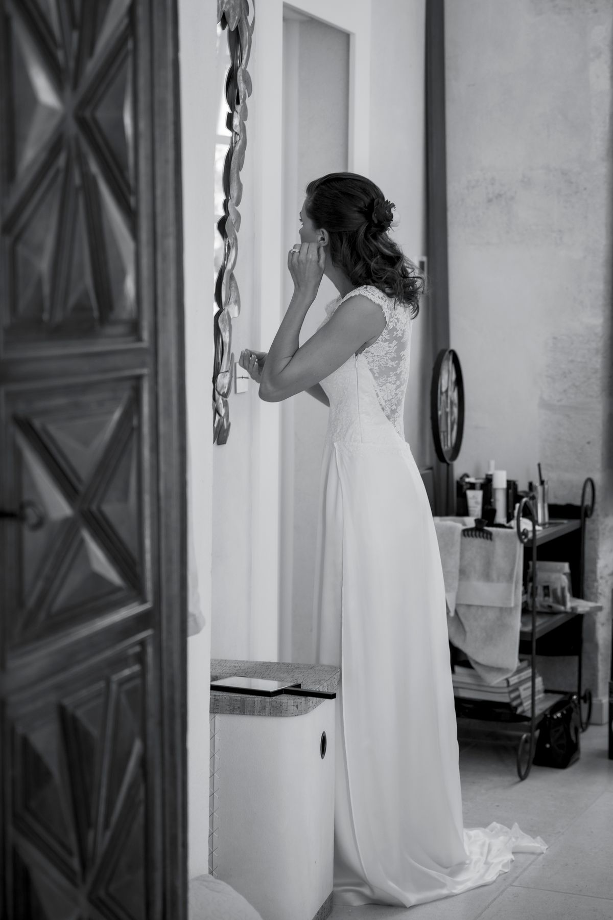 A bride getting ready, adjusting an earring in front of a mirror
