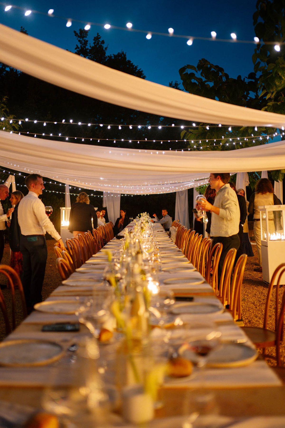 Long-table evening reception under festoon lights and draped fabric at Domaine de Blacailloux