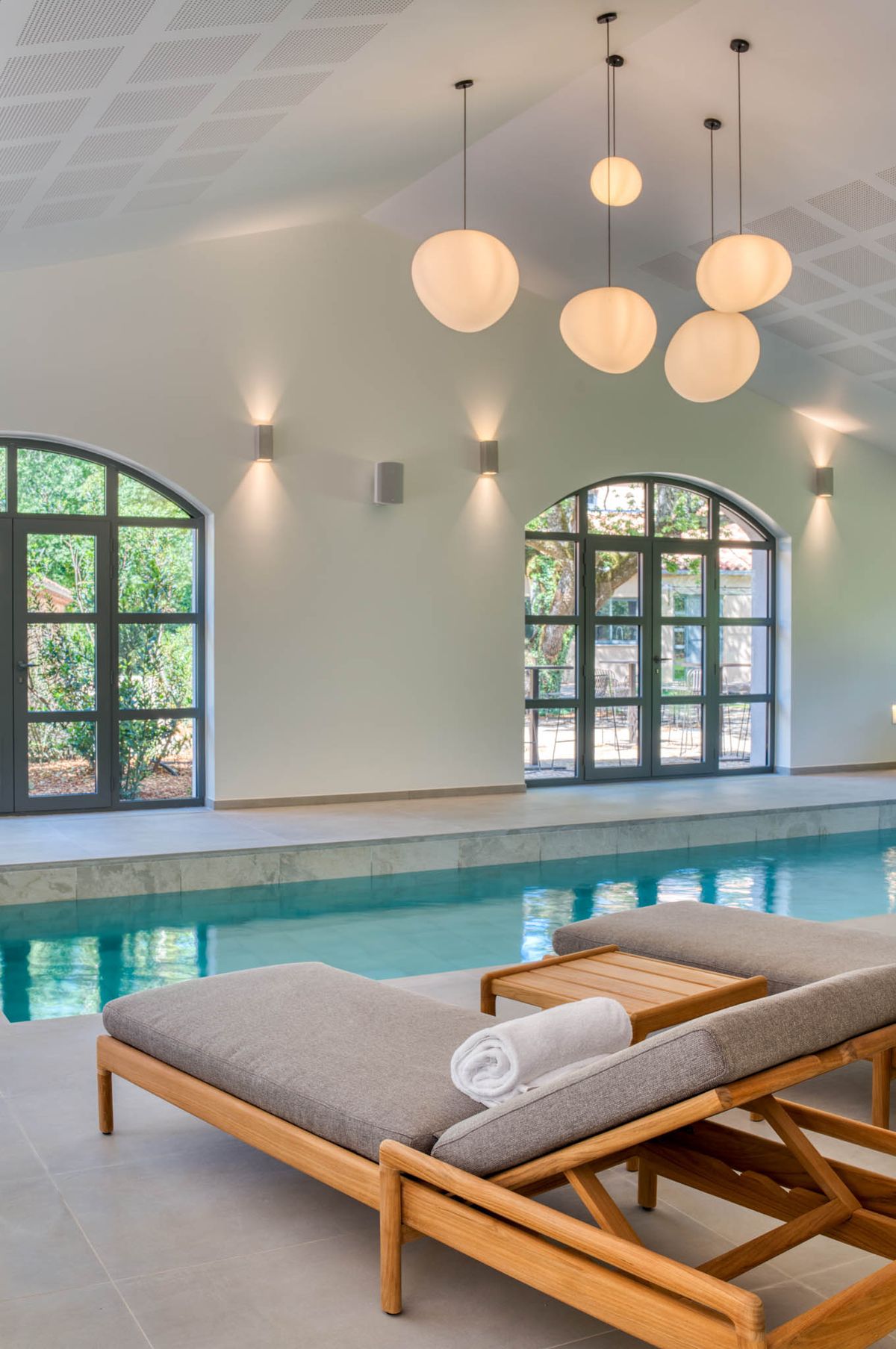 Indoor heated pool with arched windows and globe pendant lights at Domaine de Blacailloux