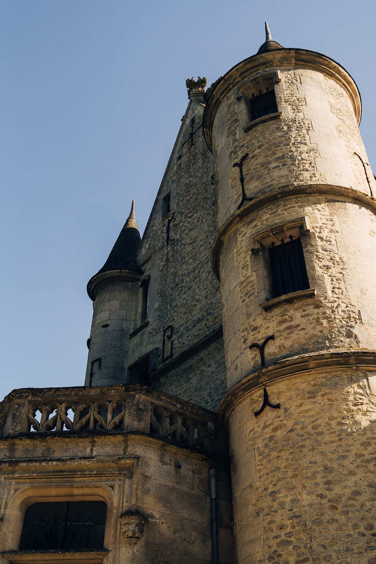 A round stone tower and slate-capped turret of the château, seen from below against a clear blue sky