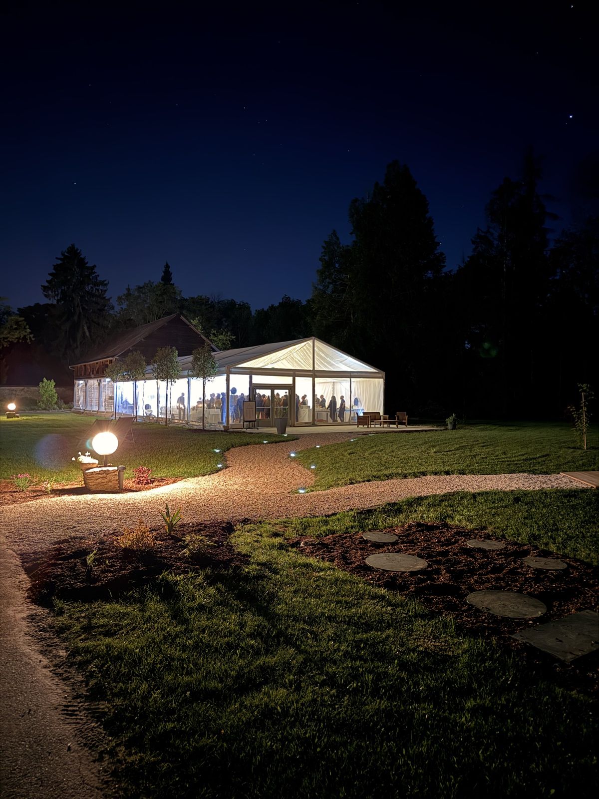 The Pavillon du Parc at night, its timber barn and glass-walled marquee full of guests beyond a lit gravel path