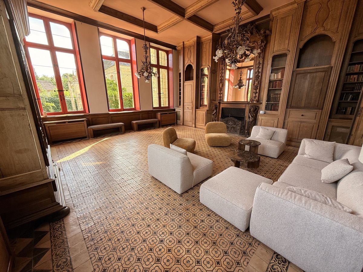 The Dumas salon with oak panelling, built-in bookcases, a carved chimneypiece and cream sofas on patterned tiles