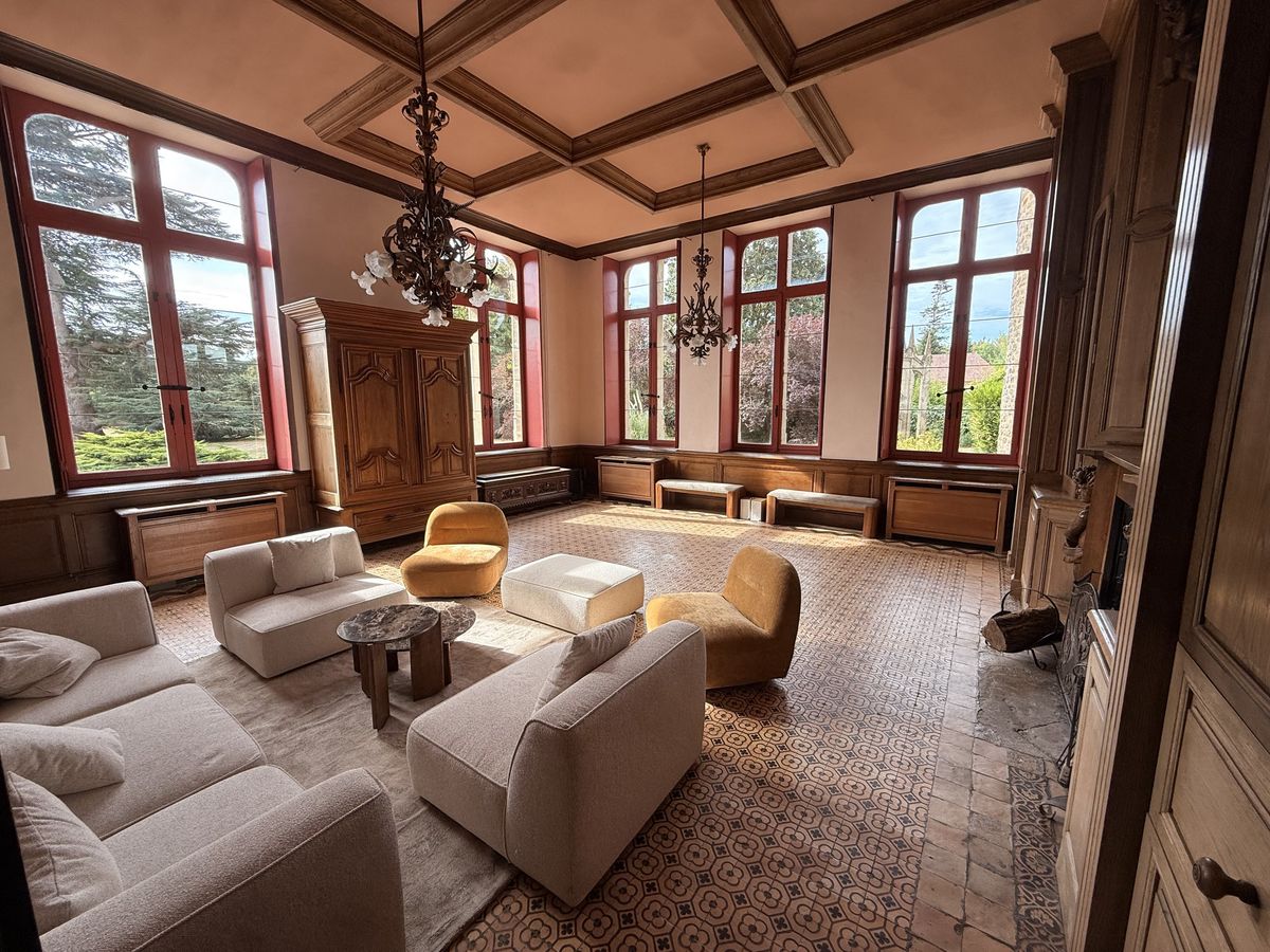 Tall red-framed windows in the Dumas salon looking onto the park, with mustard and cream armchairs