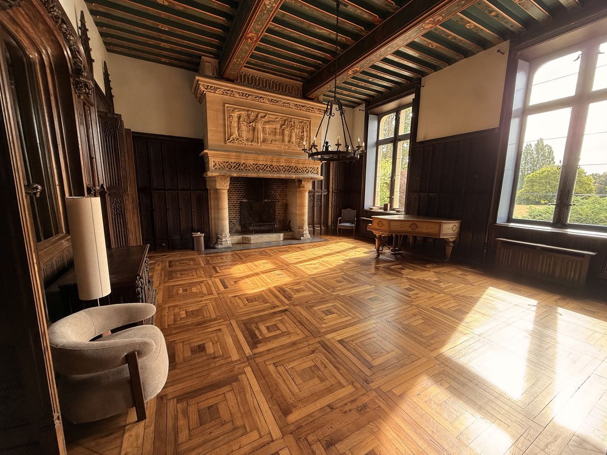 The Pulligny salon with a carved stone fireplace, painted beamed ceiling, square piano and sunlit parquet