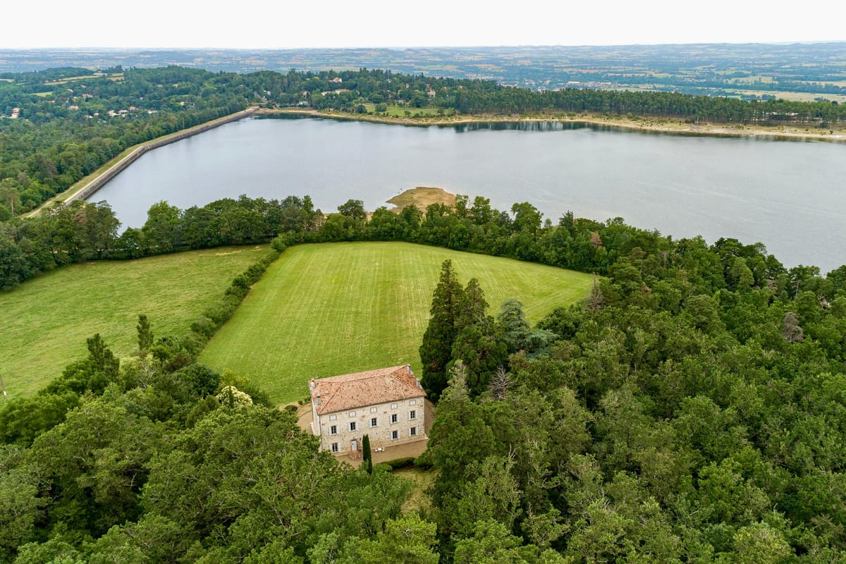 Wide aerial view of the estate, the château among trees below its meadow and the lake