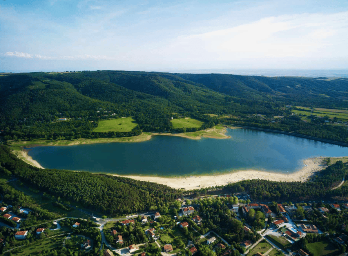 Aerial view of a lake with sandy shores, wooded hills and a village below
